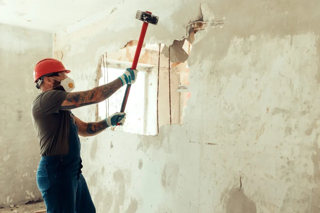 builder with a hammer in his hands breaks the cement wall