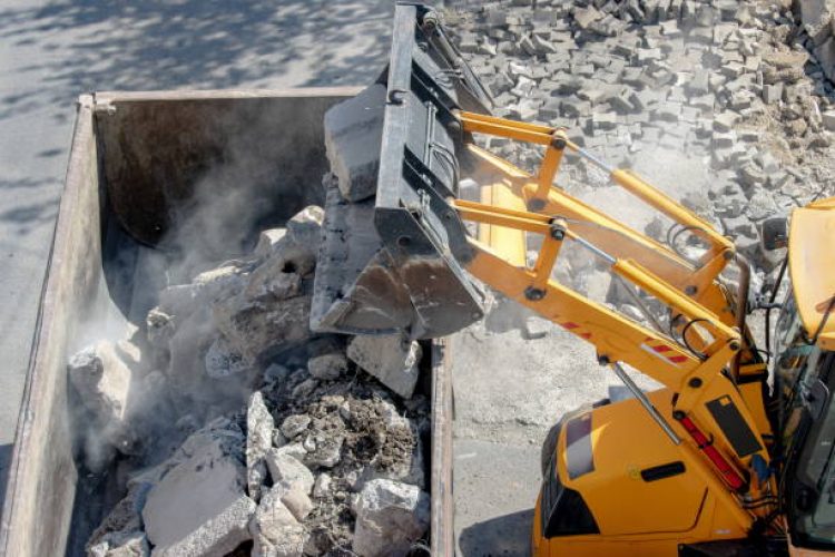 Bulldozer loader uploading concrete debris into dump truck at construction site