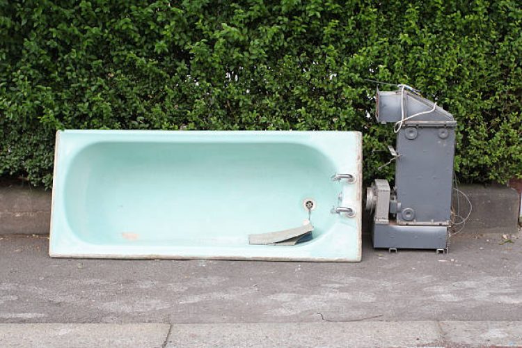 Old blue coloured bath and grey boiler on a pavement