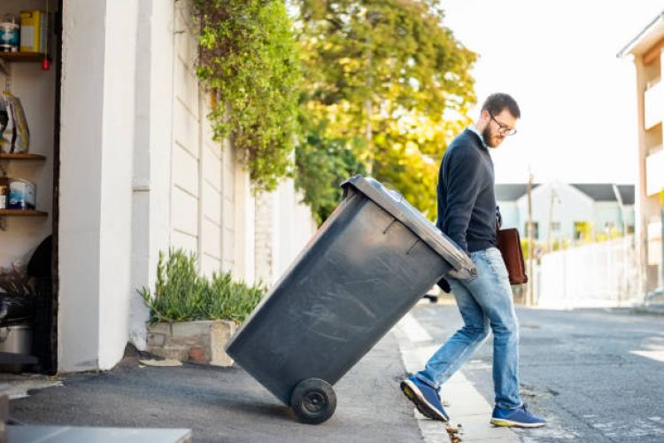 Man pulling a wheeled dumpster out of his garage while going to work
