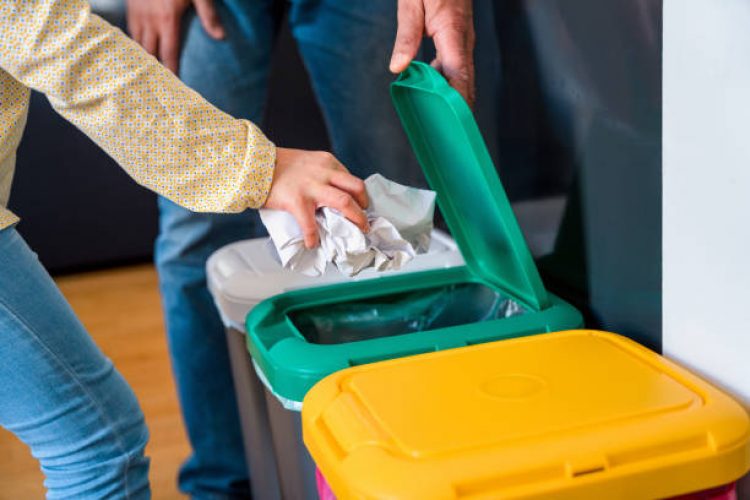 Mixed race father and daughter are putting paper into a garbage bin at home. They are recycling trash.