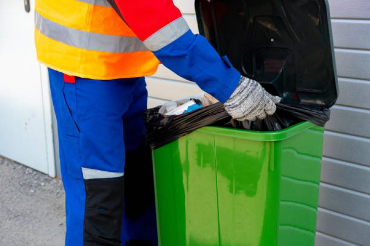 Janitor takes garbage out of trash container outdoors in the street