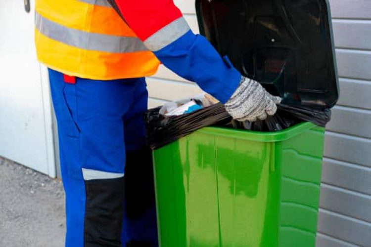 Janitor takes garbage out of trash container outdoors in the street