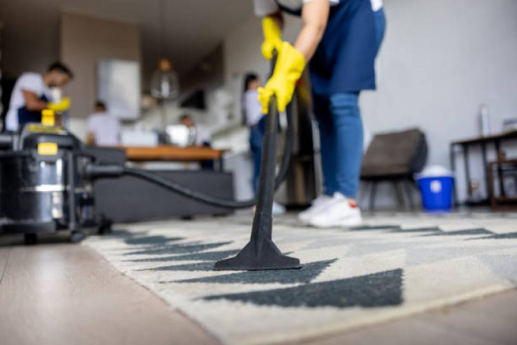 e5 Close-up on a professional cleaner vacuuming a carpet while working at an apartment - housework concepts
