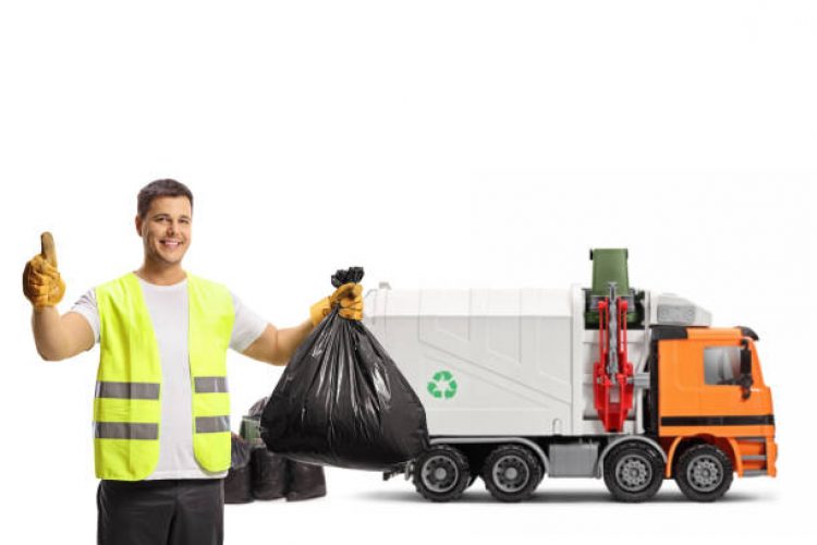 Waste collector with a garbage truck holding a plastic bin bag and showing thumbs up isolated on white background