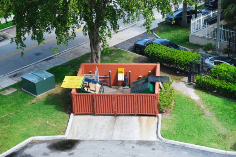 e9 Dumpster half-filled with garbage next to residential area, road and parking lot behind commercial building aerial street view photo. Waste management concept.