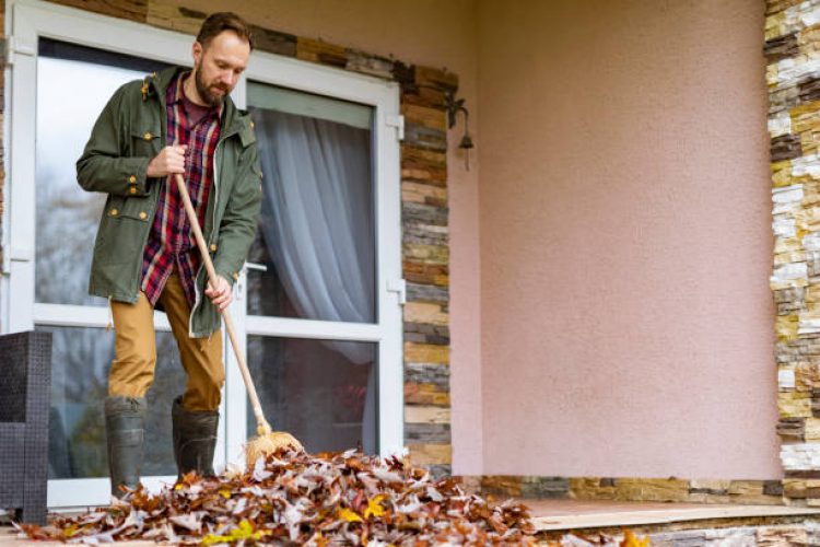 Adult man sweeping autumn leaves from porch
